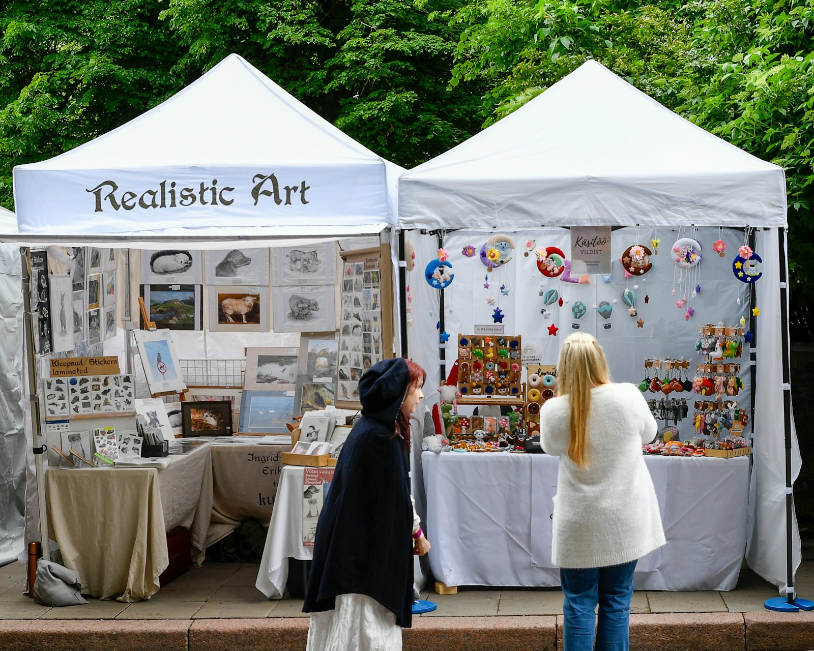 Two white 10 by 10 vendor tents at an outdoor art market, one with a banner across the top