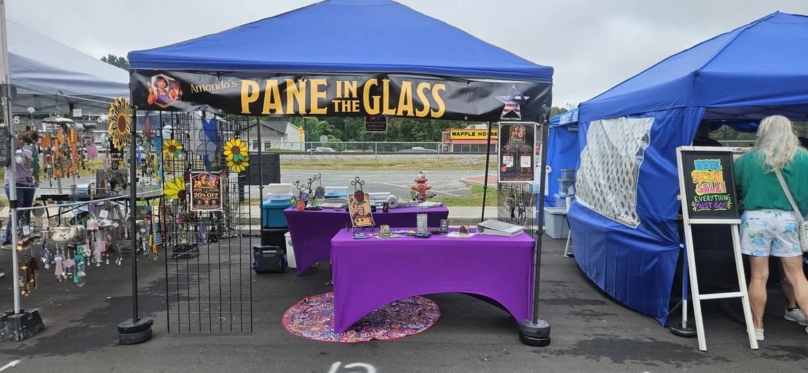 A vendor's blue 10 by 10 canopy at an outdoor market with a 10 foot by 1 foot banner tied across the front frame